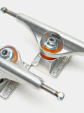 Close-up of two metal skateboard trucks with orange bushings on a clean white background.