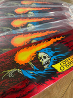 A close-up of a skateboard deck wrapped in clear plastic, showing a graphic of a hooded skeleton holding a flaming ball of fire. The deck has a red background with black, blue, orange, and yellow artwork, and the text 'COREY O'BRIAN' is visible on the right side.