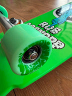 Close up of wheels - Santa Cruz Rob Roskopp One Old School complete skateboard with a bright green deck, silver trucks, matching green wheels, and a circular black-and-white graphic featuring a blue arm breaking through the centre. 'ROB ROSKOPP' Branding.