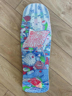 A skateboard deck with a highly detailed, colorful underwater illustration featuring a stingray, sea urchins, coral, and a red fish, photographed flat on a light brown wooden floor.